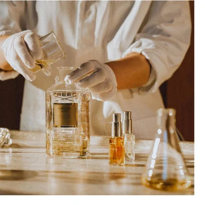 Hand holding a Creed Aventus Cologne perfume bottle with text reading CREED and AVENTUS COLOGNE.
