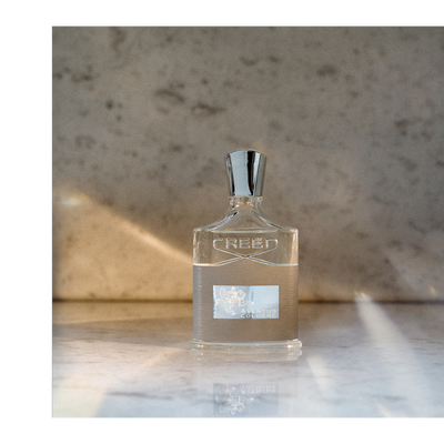 A Creed Aventus Cologne perfume bottle sits on a marble surface with the text CREED AVENTUS COLOGNE visible.