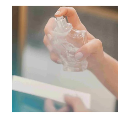 Hand spraying a clear perfume bottle with the text LOVE IN WHITE visible.