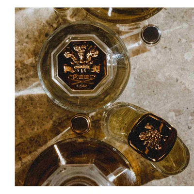 Overhead view of several perfume bottles on a textured surface with text CREED PARIS 1760 on the cap of the central bottle.