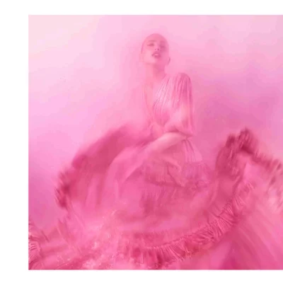 A person in a dynamic pose wearing a flowing pink dress with ruffled layers against a pink background.