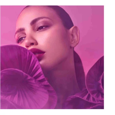 Close-up portrait of a person in a magenta ruffled garment with dramatic eye makeup and dark lipstick, looking up and away against a pink background.