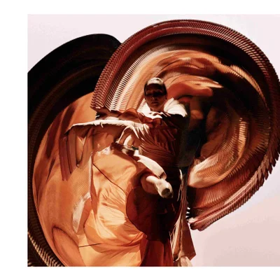 A person wearing an intricate orange pleated costume with large fan-like structures around their body.