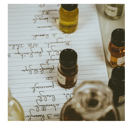 A close-up of several small bottles on a sheet of lined paper with handwritten text listing ingredients including Bergamote S/B Italie 5 Phenylacetique Muguet Phenyl CD Paracresol linalool citronellyl ao 3 Hoxenyl and text on bottle labels including ENCE 24 214.