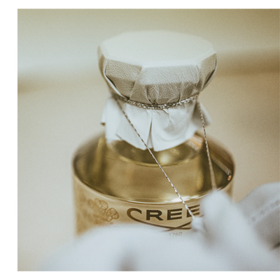 Overhead view of several perfume bottles on a textured surface with text CREED PARIS 1760 on the cap of the central bottle.