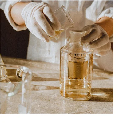 Hand holding a glass perfume bottle with amber liquid and a gold cap featuring the text Royal Princess Oud and CREED.