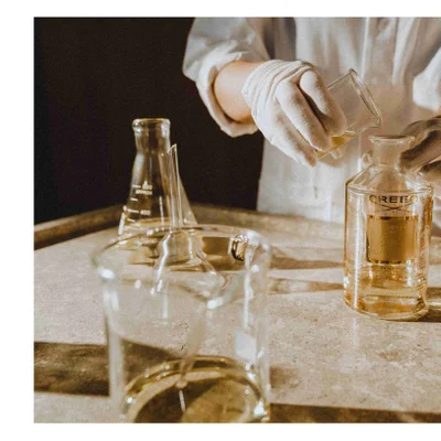 Person wearing gloves pours liquid from a beaker into a glass bottle with the label CREED Millesime Imperial 1760.