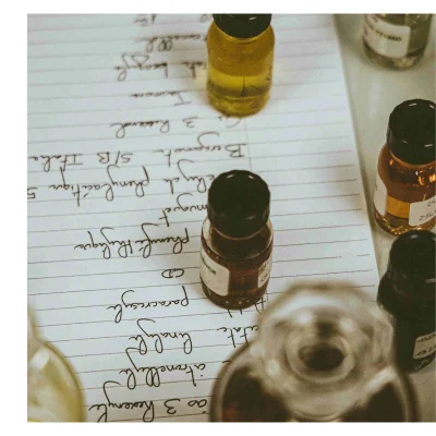 A close-up of several small bottles on a sheet of lined paper with handwritten text listing ingredients including Bergamote S/B Italie 5 Phenylacetique Muguet Phenyl CD Paracresol linalool citronellyl ao 3 Hoxenyl and text on bottle labels including ENCE 24 214.