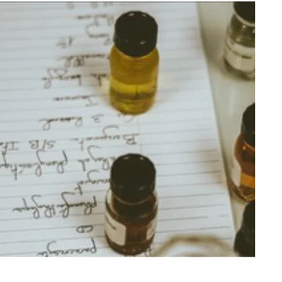 Several small glass bottles with black caps containing yellow and dark brown liquids are placed on a sheet of lined paper with handwritten notes, including the visible text Berry, Randel, Burgam, S/B IT, Bergamot, yl ilang, longleaf, plumifolia, CD, and Paracarya.