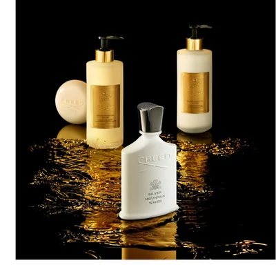 A dark bottle of Creed Absolu Aventus perfume with a rider on a horse logo, marked 75 ML 2.5FL.OZ., is tilted over two citrus fruits.