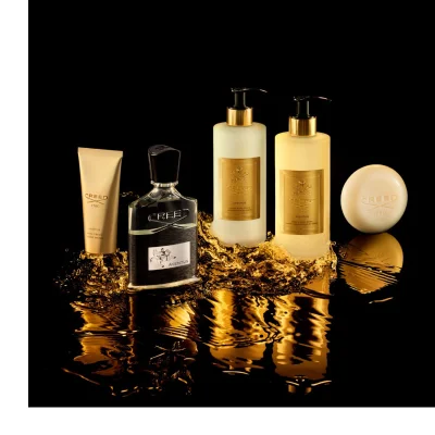 A dark bottle of Creed Absolu Aventus perfume with a rider on a horse logo, marked 75 ML 2.5FL.OZ., is tilted over two citrus fruits.