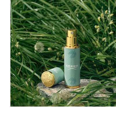 A Creed Aventus perfume bottle is shown in front of a pineapple with the text CREED AVENTUS visible on the bottle.