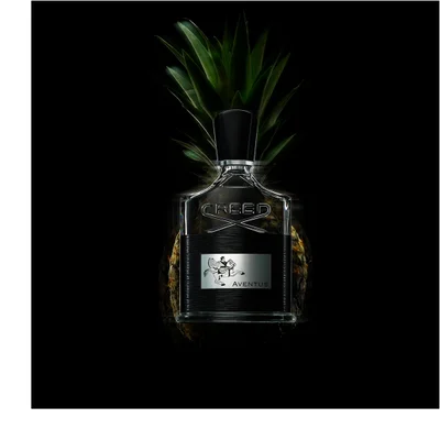 Creed Aventus bottle centered against black background with pineapple behind, creating a dramatic, bold fragrance visual.